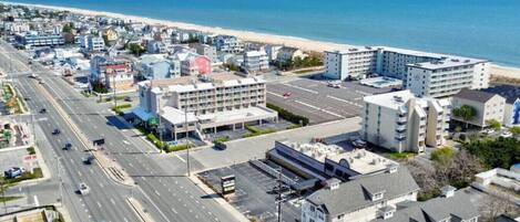 A coastal cityscape with a wide road, beachfront buildings, and a large hotel with multiple floors and balconies.