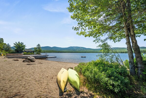 A lakeside beach with two canoes, a dock, and a forested area. - Saddleback Lake Lodge 06 | Close to Saddleback (Rangeley)