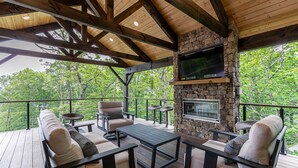 Una terraza al aire libre techada con paredes de piedra, un televisor de pantalla plana y mobiliario exterior.