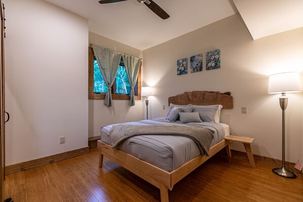 Un dormitorio con cama de madera, una lámpara de pie y una ventana con cortinas.