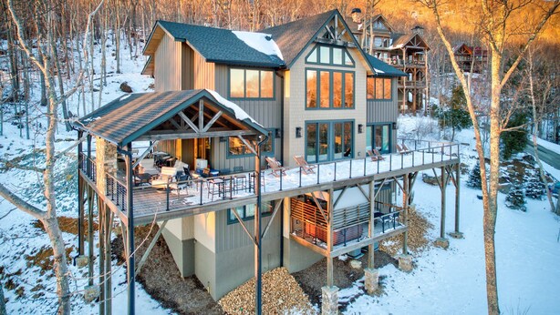 Una cabaña grande de madera, de varios pisos, con terraza, rodeada de árboles y nieve.