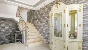 Eine Treppe mit Metallgeländer, die zu einer Zwischenebene führt, ein weißes Schränkchen mit Glastüren und ein Fliesenboden.