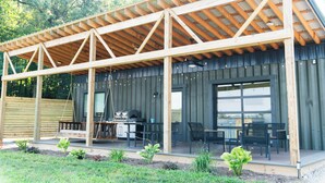 Une terrasse extérieure couverte, équipée d’un barbecue, de sièges et offrant une vue sur la végétation environnante.