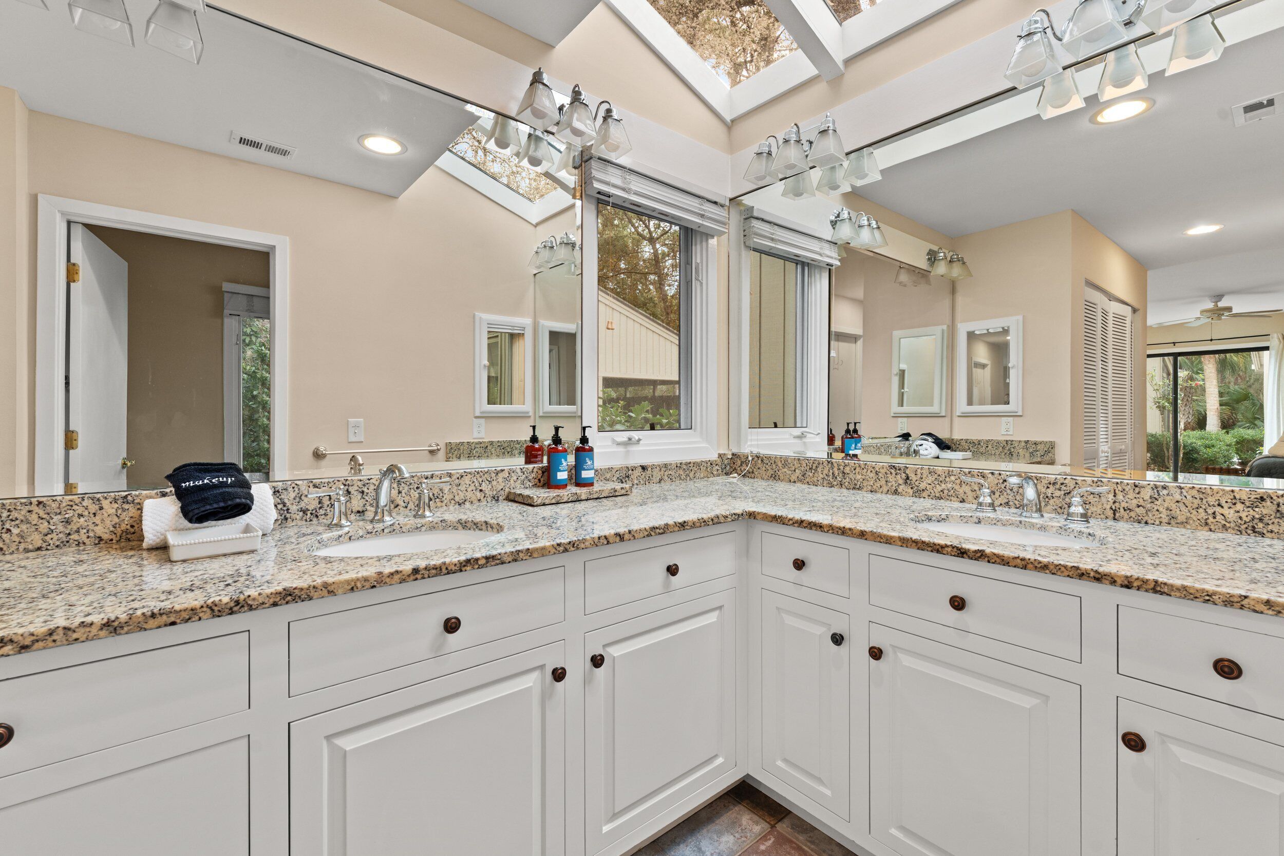 A bathroom with a large mirror, granite countertop, and white cabinetry.