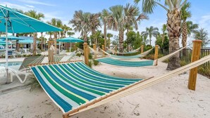 A beach area with hammocks, palm trees, and a pool.