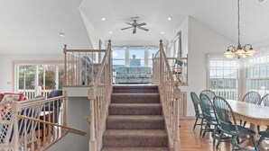 A staircase leading to a balcony with a view, a dining area with chairs, and a ceiling fan. - 1285 - Sands to Sea - Pet-Friendly Corolla Retreat Near the Beach (Corolla)