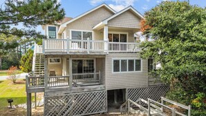 A two-story house with a balcony, a covered porch, and a wooden deck. - 1285 - Sands to Sea - Pet-Friendly Corolla Retreat Near the Beach (Corolla)