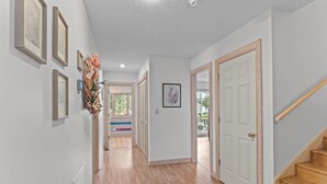 A hallway with wooden flooring, white walls, and a staircase with a wooden handrail. - 1285 - Sands to Sea - Pet-Friendly Corolla Retreat Near the Beach (Corolla)