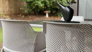 A patio with two white mesh chairs and a black vase with green foliage. - Creek Front House (Valley View)