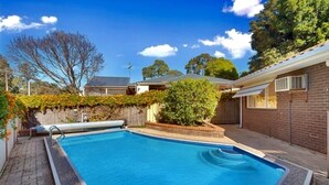 A rectangular swimming pool with a tiled edge, surrounded by a brick patio and a wooden fence. - Creek Front House (Valley View)