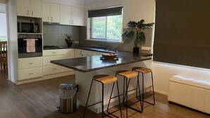 A modern kitchen with a central island, bar stools, a microwave, and a sink. - Creek Front House (Valley View)