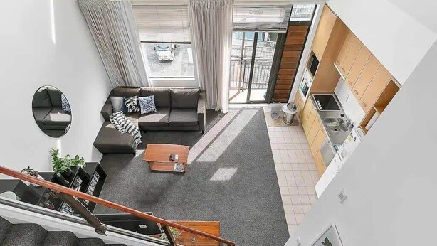 A modern apartment with a staircase, a living room with a sofa and coffee table, a kitchen, and a large window. - Roomy Loft with Free Parking by Zodiak Stays (Auckland)