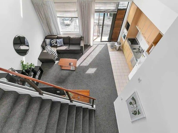 A modern apartment with a staircase, a living room with a sofa and coffee table, a kitchen, and a large window.