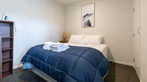 A bedroom with a bed, a bedside table, a lamp, a wall-mounted artwork, and a wardrobe. - Roomy Loft with Free Parking by Zodiak Stays (Auckland)