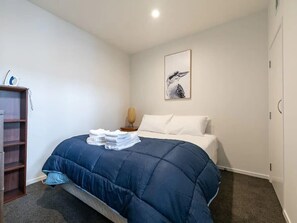 A bedroom with a bed, a bedside table, a lamp, a wall-mounted artwork, and a wardrobe.