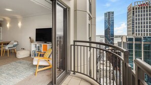 A modern apartment with a balcony, a TV, a dining area, and a view of city buildings. - Bright 1 Bedroom Beauty with Balcony Zodiak Stays (Auckland)