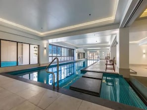 Ein Innenpool mit freiem Blick auf das Pool-Areal, einem Kachelboden und einer langen Sitzgelegenheit am Pool.