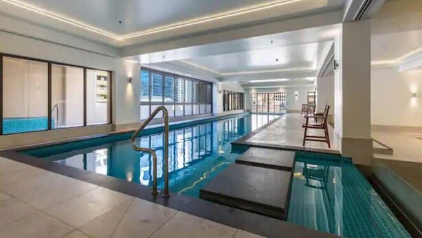 An indoor swimming pool with clear water, tiled flooring, and a modern design. - Bright 1 Bedroom Beauty with Balcony Zodiak Stays (Auckland)