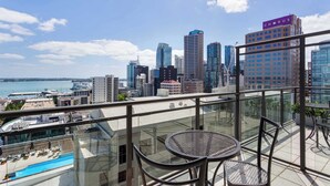 Un edificio de gran altura con un horizonte urbano de fondo, un área de piscina y un balcón con sillas y una mesa.