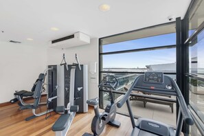 A gym with exercise equipment, a treadmill, and a large window offering a city view.