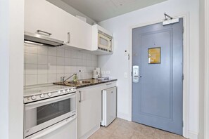 A compact kitchen with white cabinetry, a built-in microwave, a stove, and a small refrigerator.