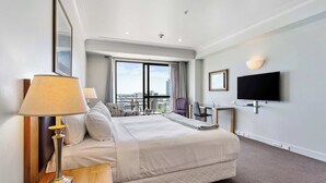 Habitación de hotel con cama, escritorio, silla, televisión y vista de la ciudad.