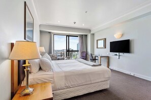 A hotel room with a bed, a desk, a chair, a TV, and a view of the city.