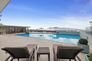 A rooftop pool area with lounge chairs, umbrellas, and a clear blue sky.