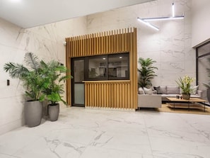 Un hall d’entrée moderne avec un comptoir de réception, un sol en marbre et des plantes en pot.
