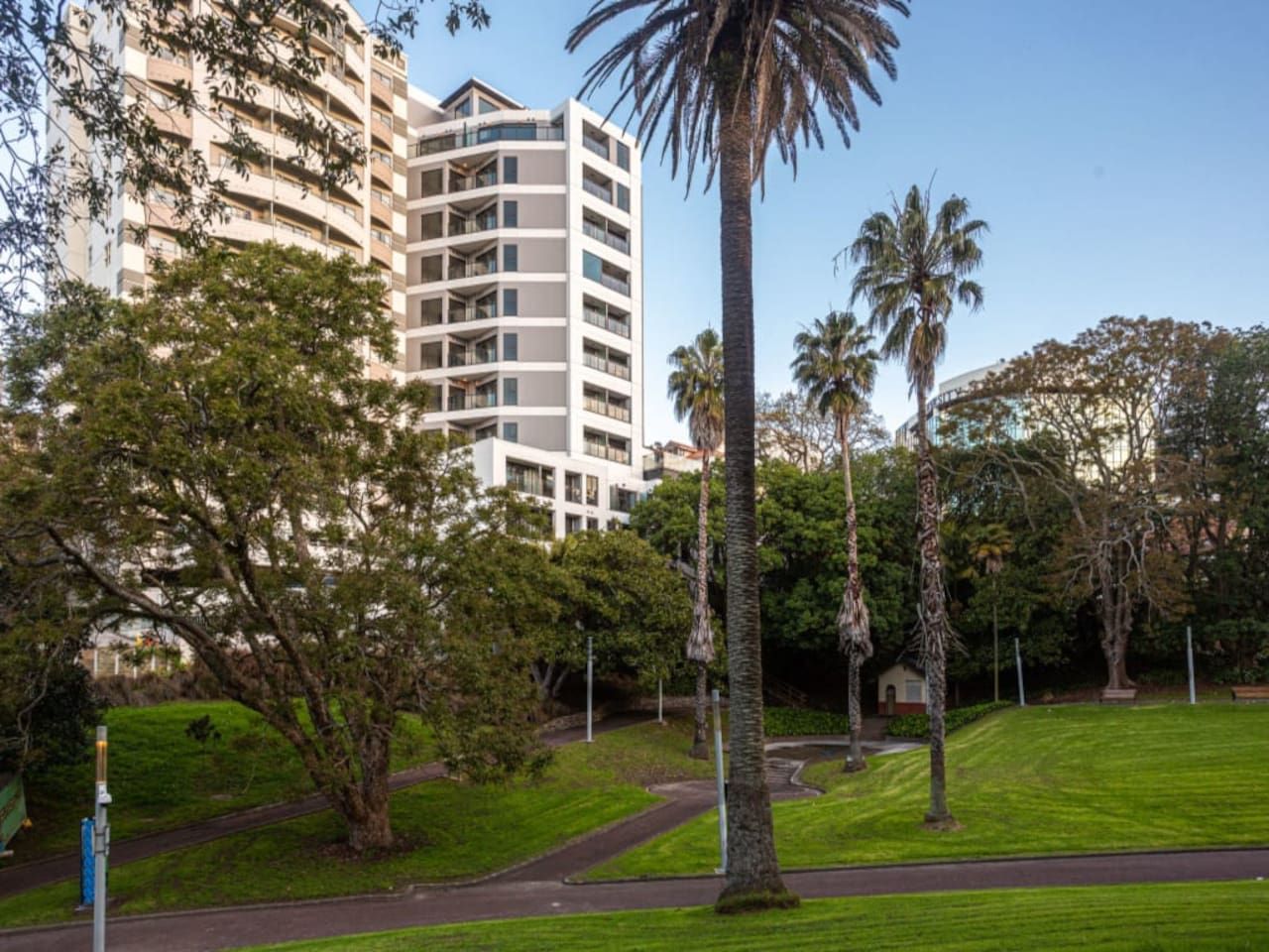 A multi-story building with a modern architectural design, surrounded by a well-maintained park with trees and a clear sky.