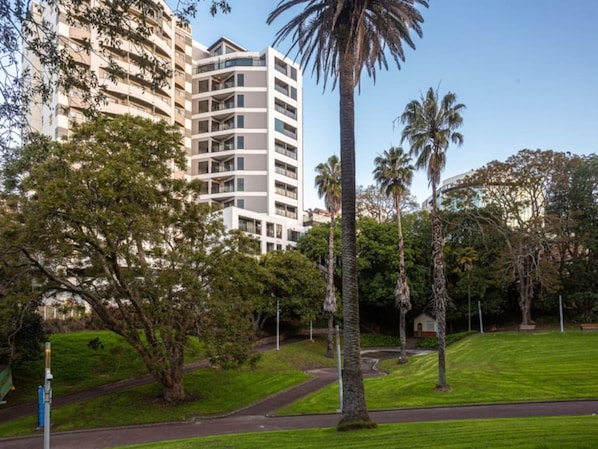 Un immeuble à plusieurs étages doté d’une architecture moderne, entouré d’un parc bien entretenu, avec des arbres et un ciel dégagé.