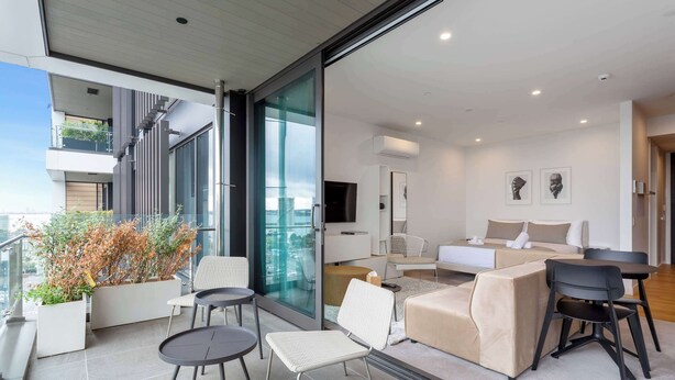 A modern living room with a sofa, chairs, a TV, and a balcony with plants. - Sleek Modern Studio with Balcony by Zodiak Stays (Auckland)