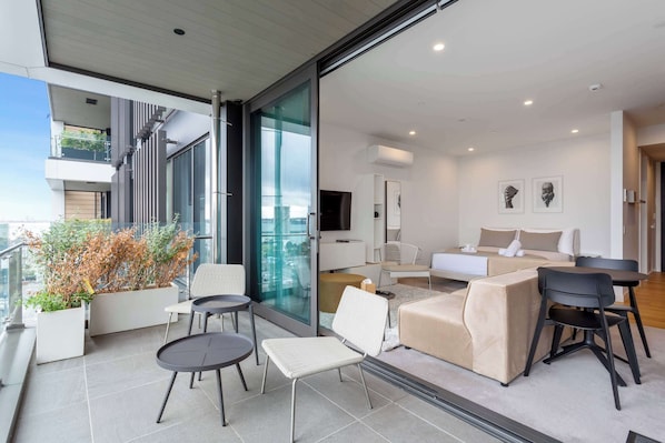 A modern living room with a sofa, chairs, a TV, and a balcony with plants.