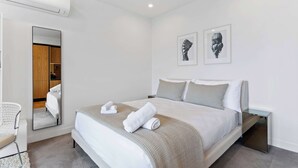 A modern hotel room with a large bed, a bedside table, a chair, a mirror, and artwork on the wall. - Sleek Modern Studio with Balcony by Zodiak Stays (Auckland)