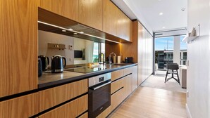A modern kitchen with wooden cabinets, stainless steel appliances, and a large window. - Sleek Modern Studio with Balcony by Zodiak Stays (Auckland)