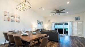 A dining area with a wooden table and chairs, a ceiling fan, and artwork on the walls.