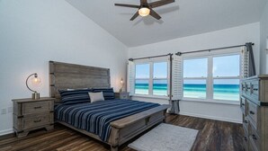 A bedroom with a wooden bed, a nightstand, a dresser, a ceiling fan, and a view of the ocean.