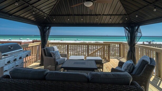 A covered outdoor deck with a grill, wicker furniture, and a view of the beach.