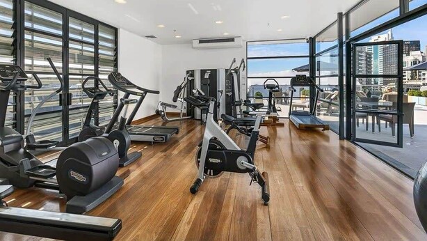Una sala de gimnàstica amb diferents aparells d'exercici, grans finestres i vistes a la ciutat.