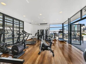 Une salle de sport équipée de divers appareils d’exercice, dotée de grandes fenêtres et offrant une vue sur la ville.