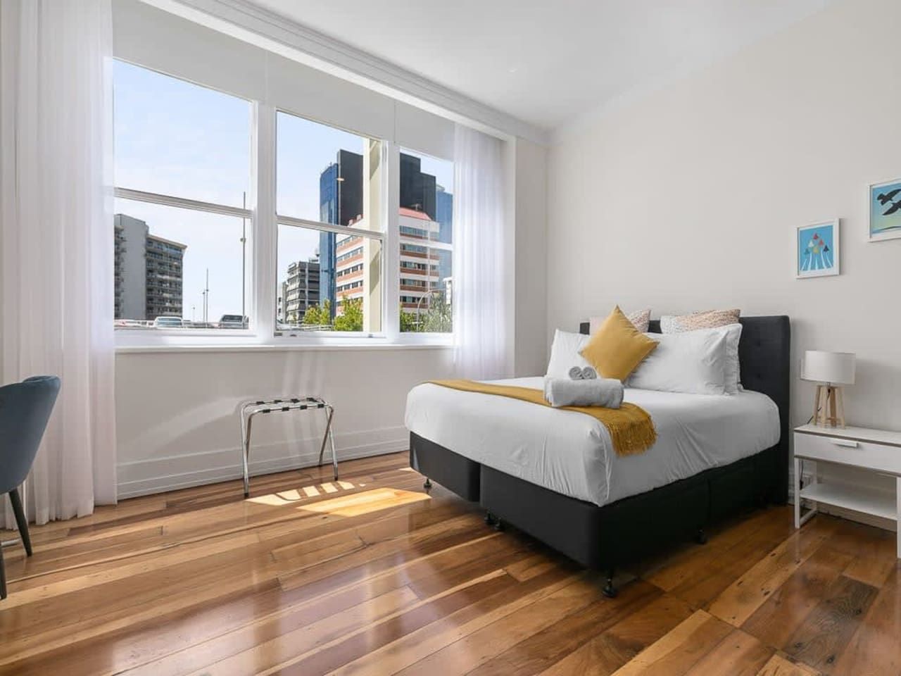 A modern bedroom with a large window, a bed, a bedside table, and a chair.