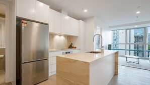Una cucina moderna con frigorifero in acciaio inossidabile, mobili bianchi, isola con piano in marmo e una grande finestra con vista sulla città.