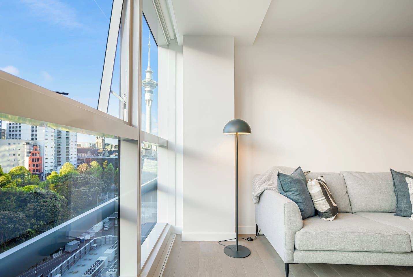 Ein modernes Wohnzimmer mit großem Fenster, einer stehenden Stehlampe und einer Couch mit Kissen.