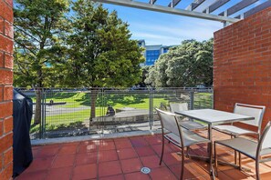 A balcony with a table and chairs, a view of a park, and a brick wall.