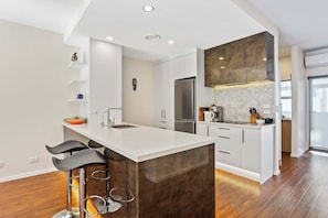 A modern kitchen with a central island, bar stools, a built-in oven, and a backsplash with hexagonal tiles.