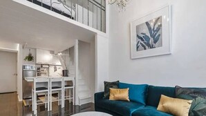 Een moderne woonkamer met een blauwgroene bank, een witte salontafel en een keuken op de achtergrond.