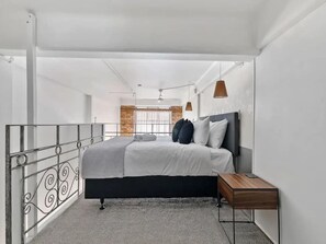A modern bedroom with a bed, bedside table, and a view of a brick wall and window. - Stylish Loft Apt in CBD w/ King Bed I Zodiak Stays (Auckland)