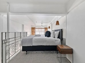 A modern bedroom with a bed, a nightstand, a hanging light, and a view of a brick wall. - Stylish Loft Apt in CBD w/ King Bed I Zodiak Stays (Auckland)