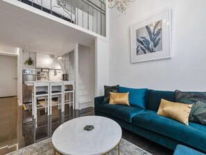 A modern living room with a teal sofa, a white coffee table, and a dining area with white furniture. - Stylish Loft Apt in CBD w/ King Bed I Zodiak Stays (Auckland)