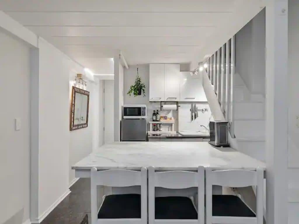 A modern kitchen with white cabinetry, a central island, and a dining area with a white table and chairs.